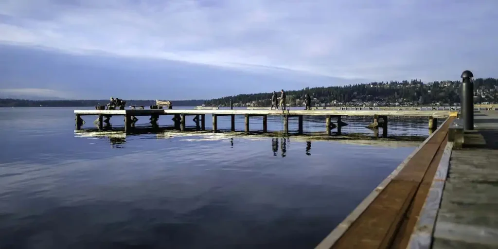 wooden pier on lake washington in kirkland with people walking, calm water, and distant tree-covered hills
