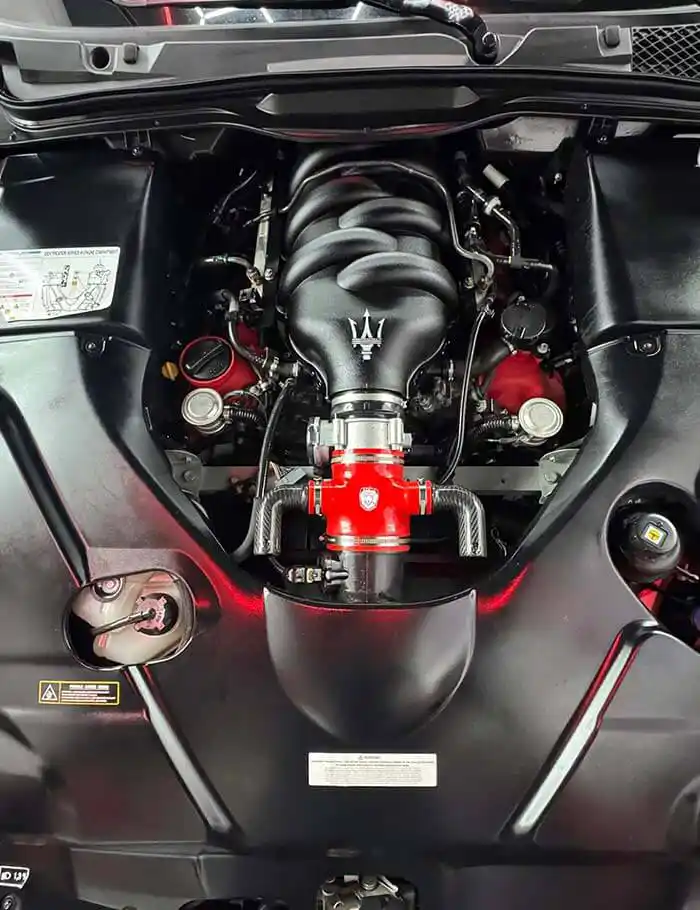 clean engine bay of black maserati with red-accented intake, supercharger pulley, and polished components